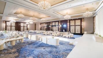 A large banquet hall with round tables, white chairs, and a blue patterned carpet.