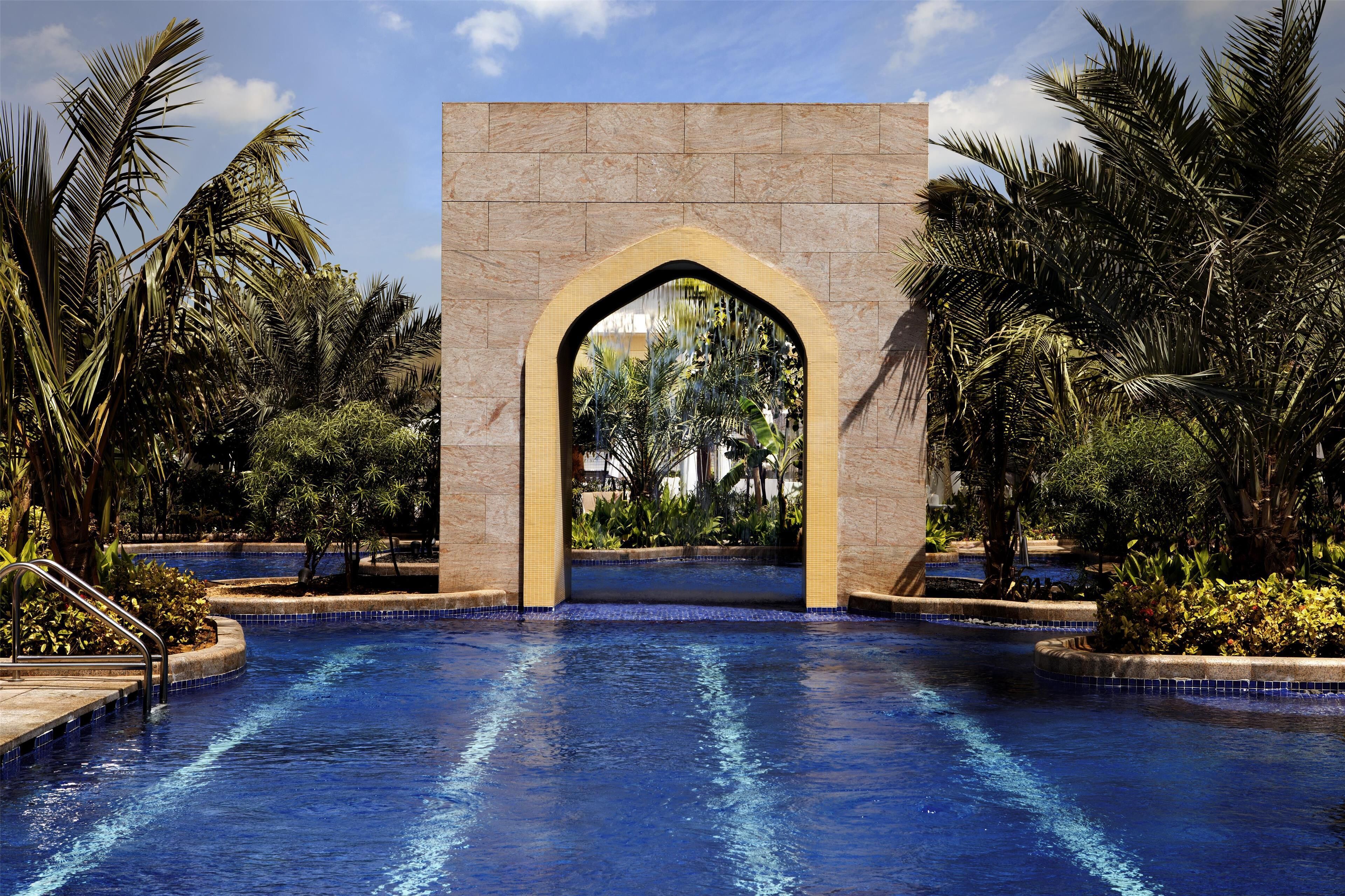 A swimming pool with a central archway, surrounded by palm trees and plants.