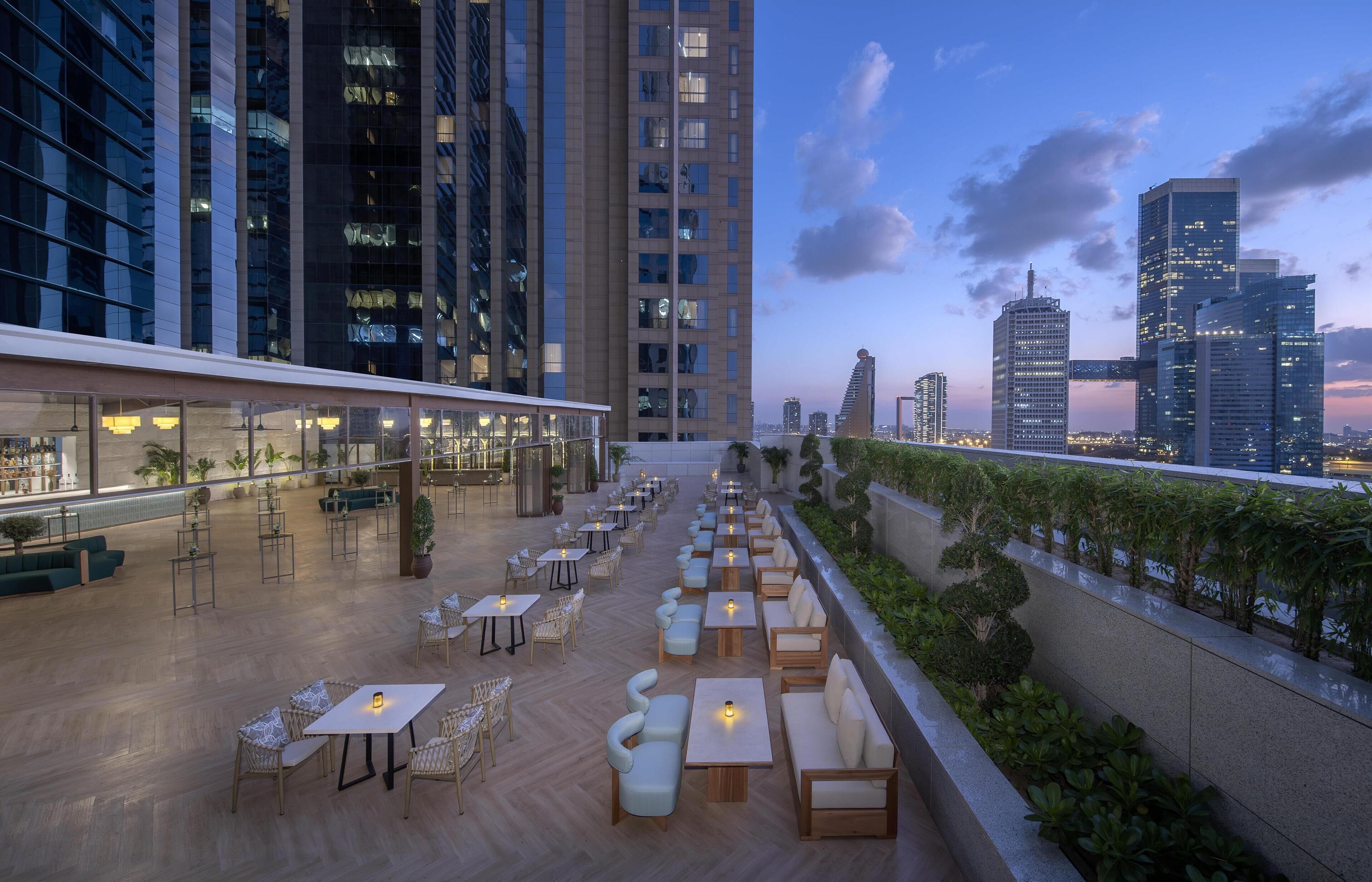 Une terrasse sur le toit avec des sièges extérieurs, une vue sur les gratte-ciel de la ville et des bâtiments modernes en arrière-plan.