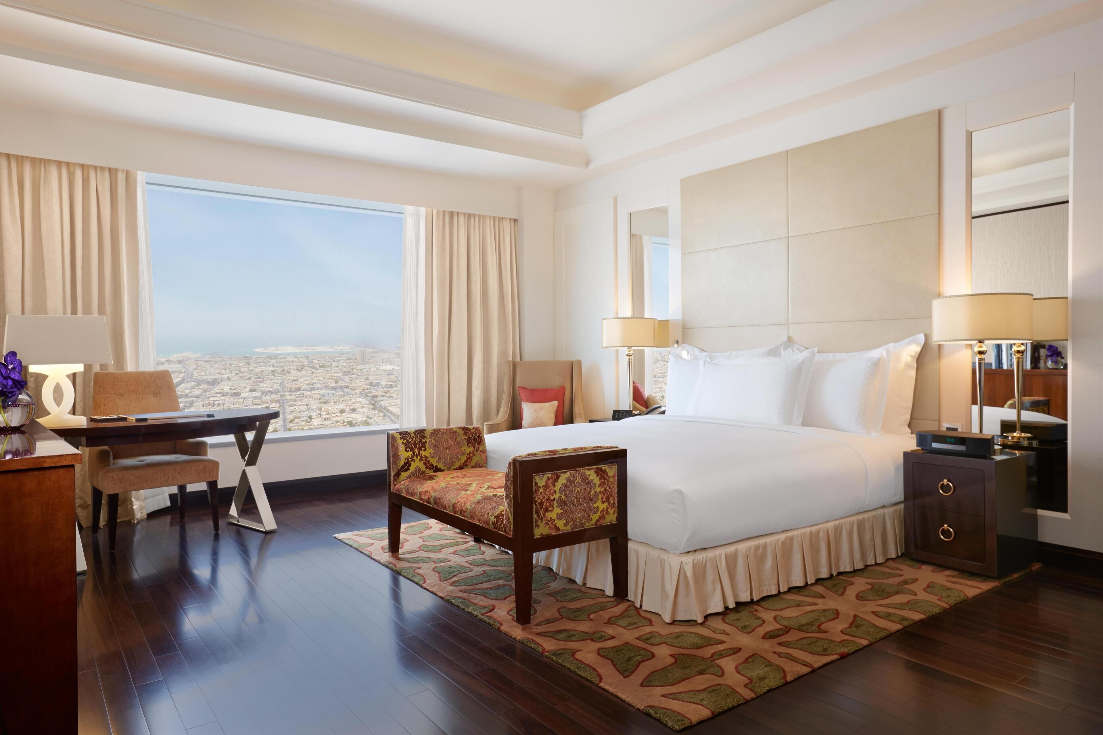 Habitación de hotel con una cama grande, un escritorio con silla, una mesita de noche y vistas a la ciudad.