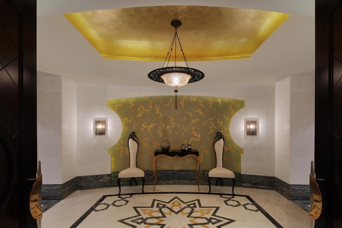 Un hall d’entrée avec un lustre, deux fauteuils, une table et des murs à motifs.