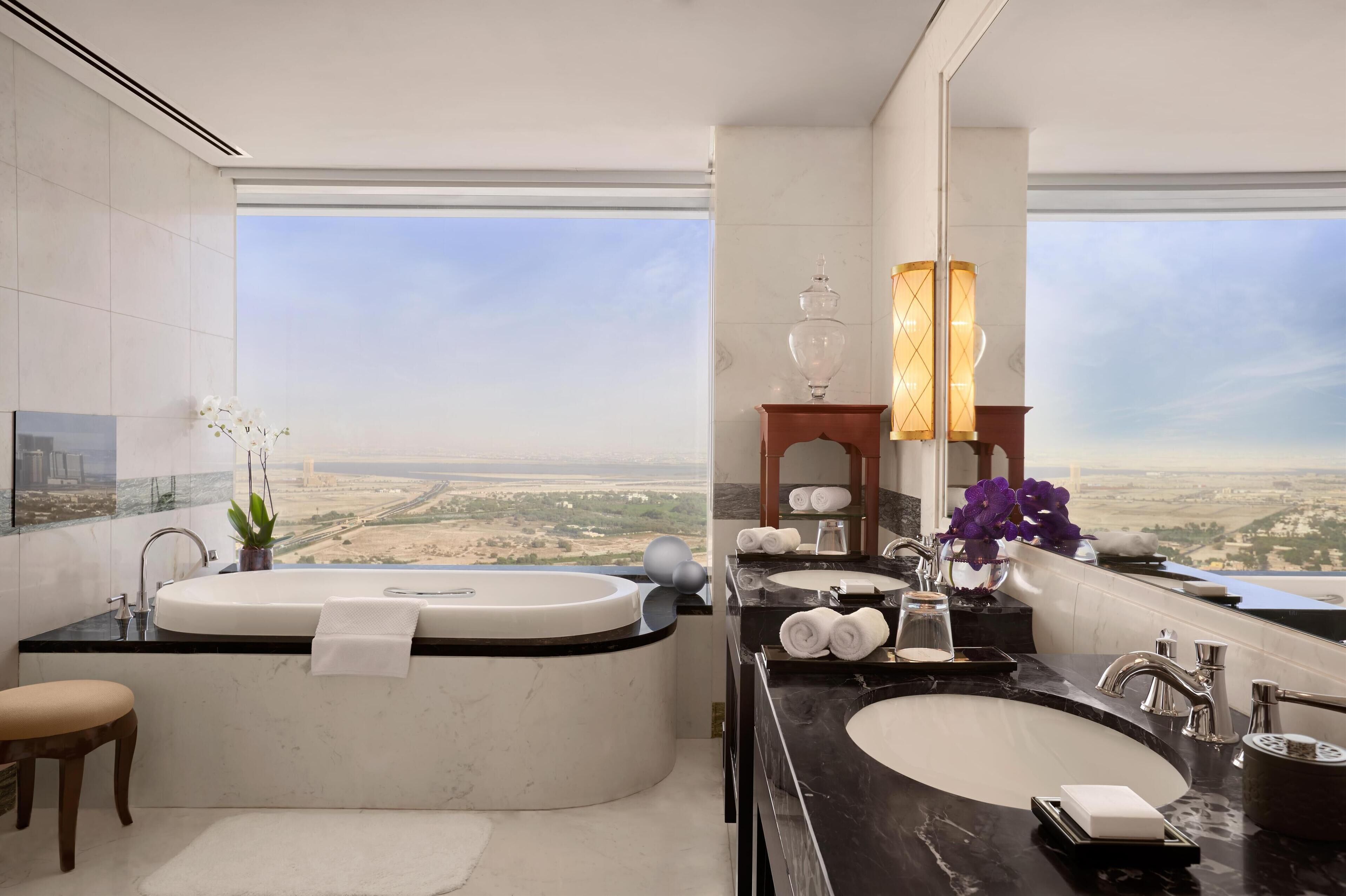 A modern bathroom with a large bathtub, two sinks, and a view of a desert landscape.
