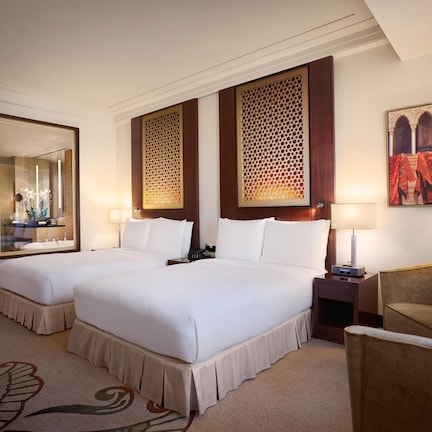 A hotel room with two beds, a desk, a chair, and a decorative mirror.
