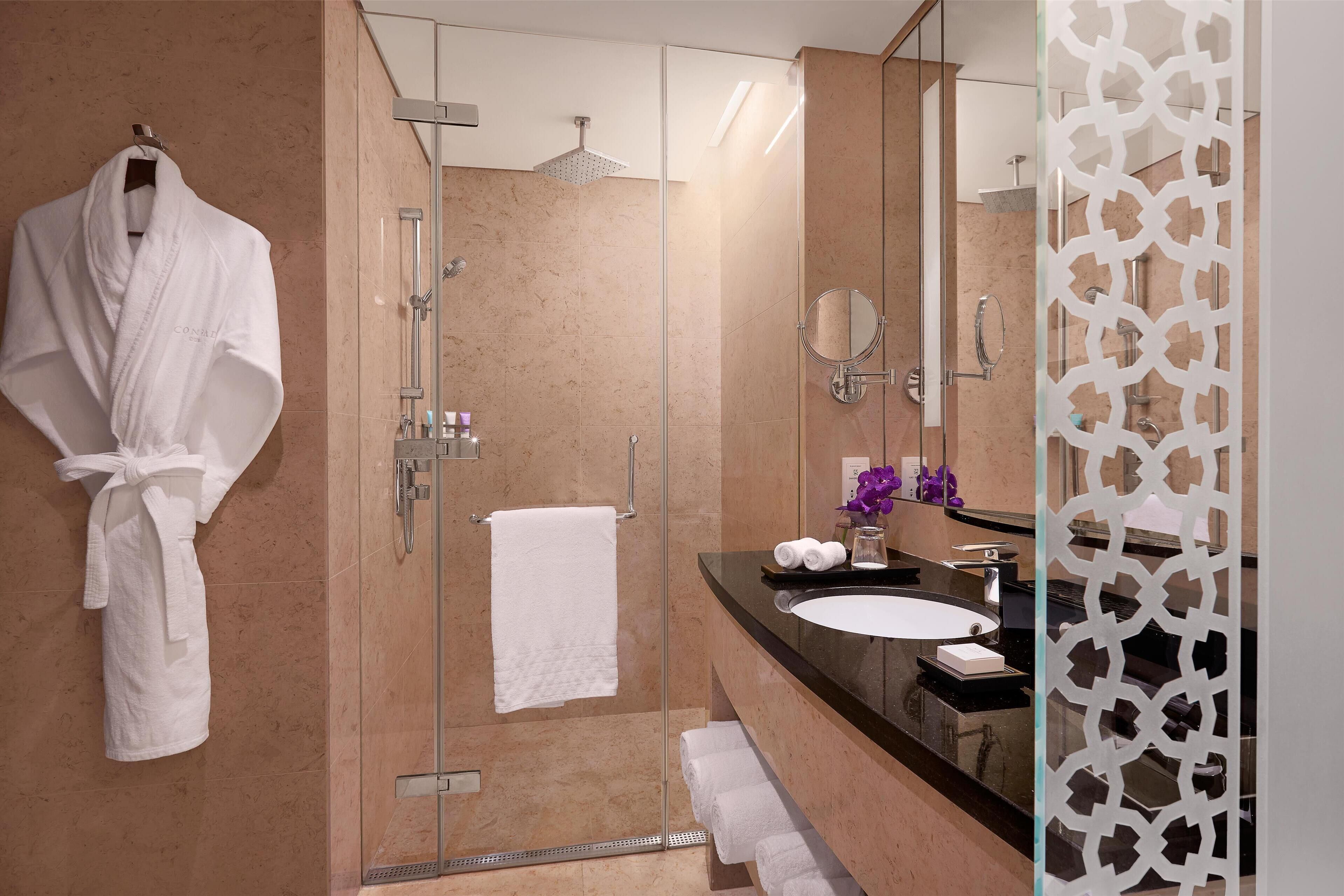 Une salle de bain moderne avec une douche à l’italienne en verre, une serviette blanche accrochée au mur et un meuble-lavabo avec un miroir et un évier.