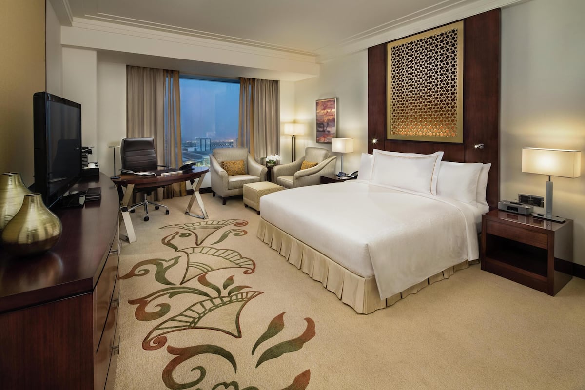 Une chambre d’hôtel avec un grand lit, un bureau avec un ordinateur, une télévision et une vue sur le paysage urbain.