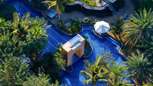 An aerial view of a resort with a central swimming pool, palm trees, and lounge areas. - Conrad Dubai (Dubai)