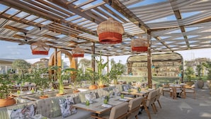 An outdoor dining area with tables and chairs, potted plants, and a bar area with shelves of bottles. - Conrad Dubai (Dubai)