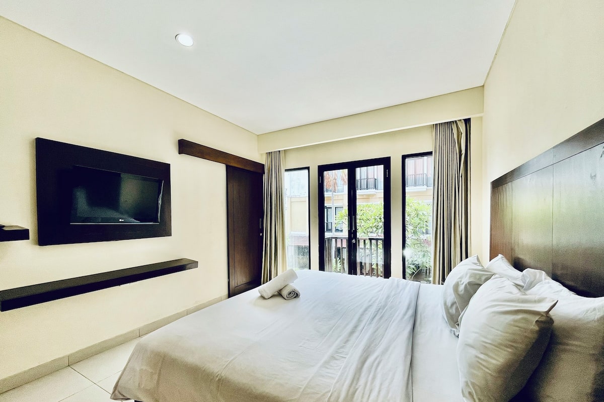 Habitación de hotel con cama, televisor de pantalla plana en la pared y ventana con cortinas.
