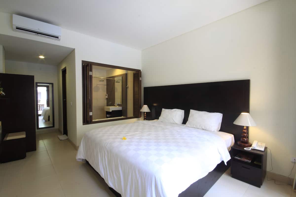Habitación de hotel con una cama grande, una mesita de noche con lámpara, un espejo y un armario.