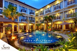 A hotel courtyard with a pool, palm trees, and outdoor seating areas. - Suris Boutique Hotel (Kuta)