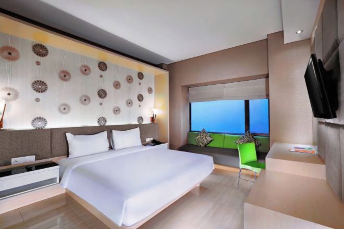 A modern hotel room with a large bed, a green chair, a flat-screen TV, and a view of the sky.