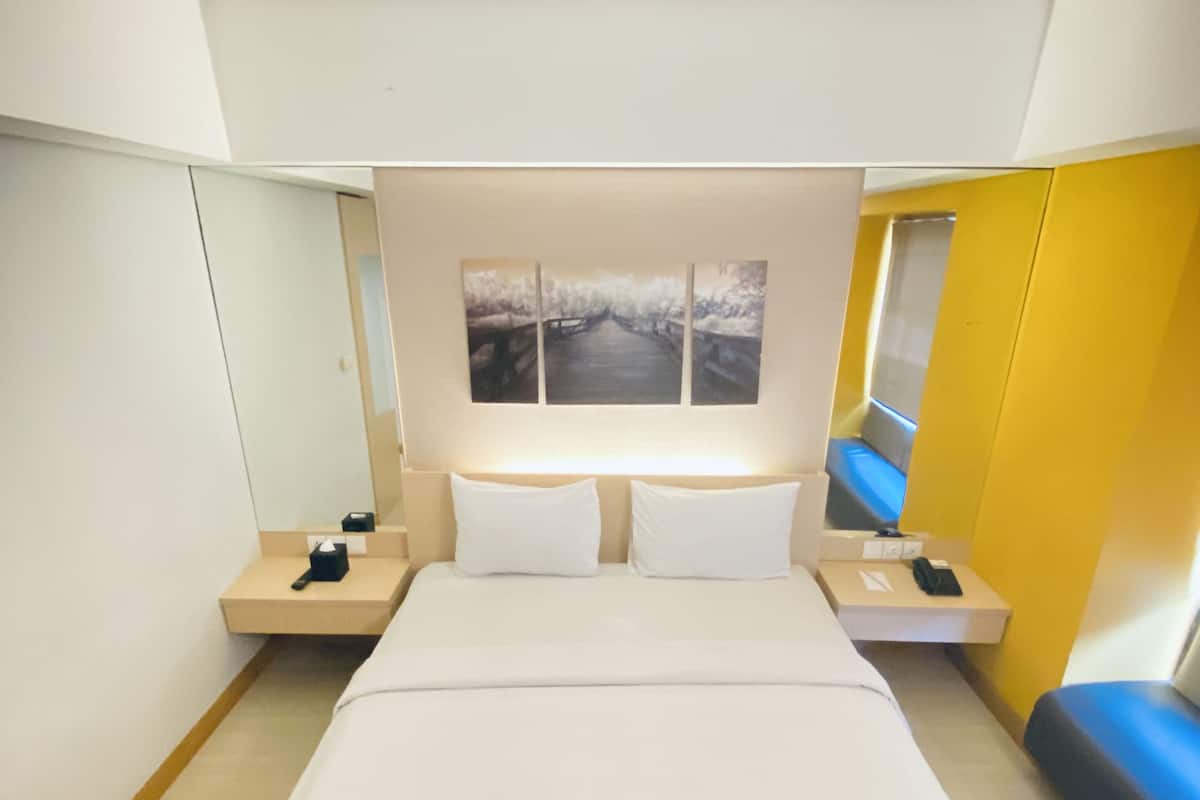 A modern hotel room with a large bed, bedside tables, a window with a view, and a small seating area.
