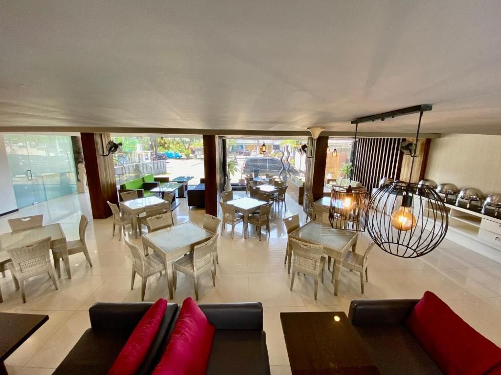 A modern hotel lobby with a central seating area, a dining section, and a view of the street.