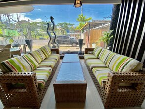 A room with wicker furniture, a central table, and a view of the street outside. - Sun Royal Hotel (Legian)