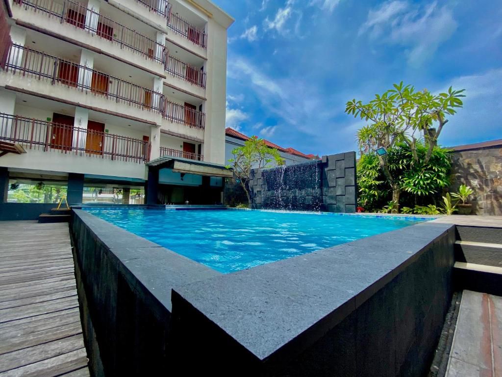 Une piscine agrémentée d’une cascade, entourée d’une terrasse en bois et bordée d’un immeuble à plusieurs étages doté de balcons.