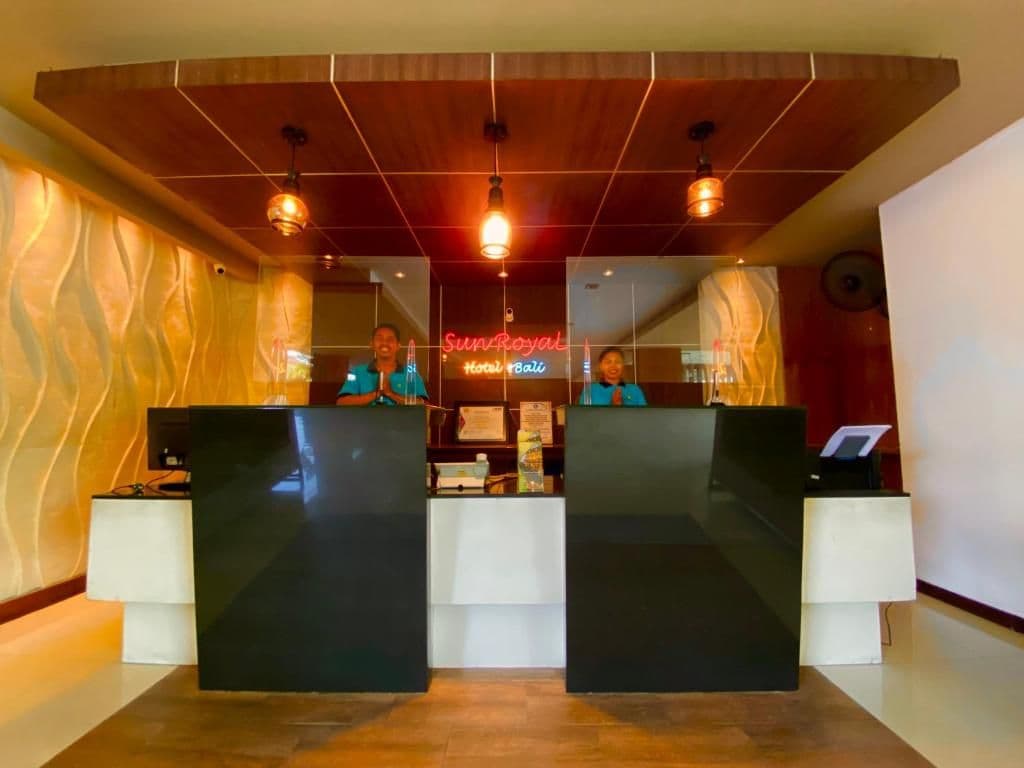 Zona de recepción de un hotel con diseño moderno, que incluye un mostrador de recepción, un letrero de neón y un techo de madera.