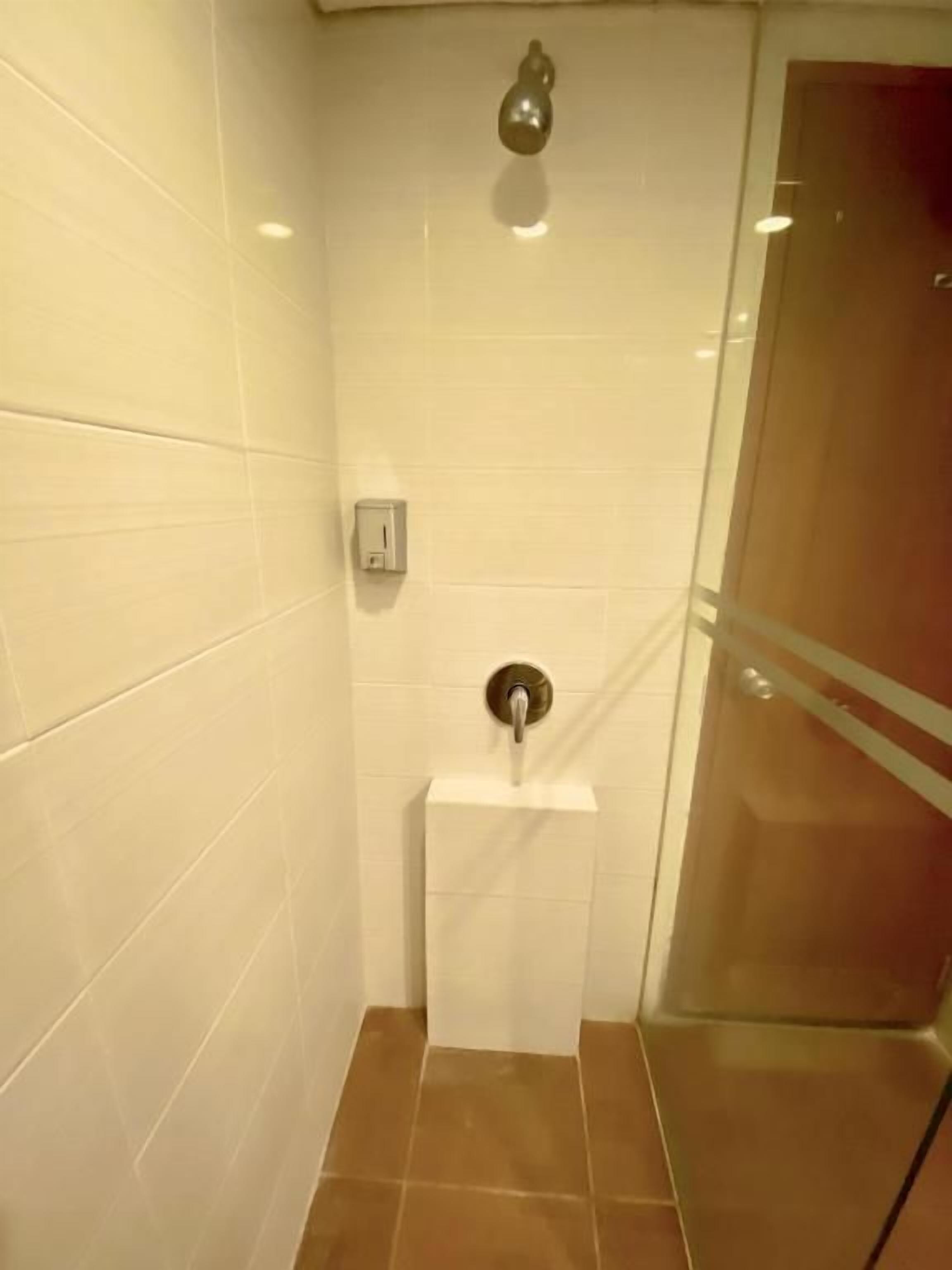 A bathroom with white tiled walls, a glass shower enclosure, and a white pedestal sink.