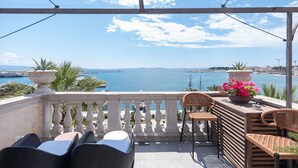 A balcony with a view of the sea, wicker furniture, and a flower vase. - Riva Luxury Suites (Split)