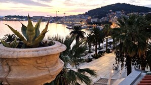 A coastal cityscape with a view of the sea, a hill in the background, and a stone planter with plants in the foreground. - Riva Luxury Suites (Split)