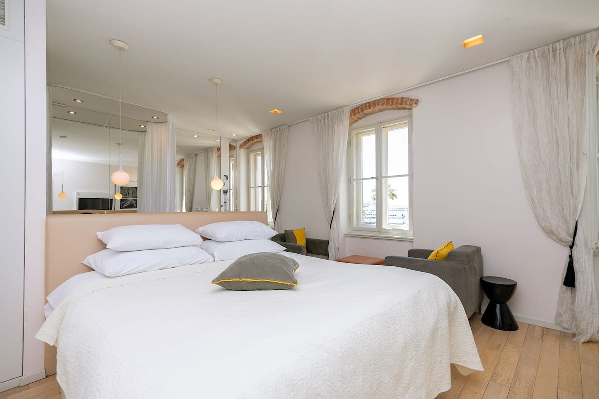 A modern bedroom with a large bed, a mirror, and a window with curtains.