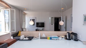 A modern hotel room with a sofa, a dining table with breakfast items, a TV, and a large window with curtains. - Riva Luxury Suites (Split)