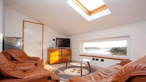 A modern living room with leather sofas, a glass coffee table, a television, and a view of a body of water through a large window. - Villa Vizula (Medulin)
