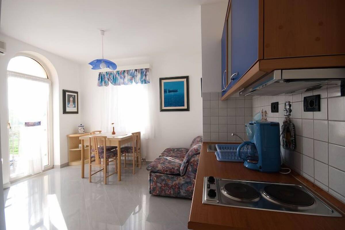 A kitchen with a dining area, a sofa, and a large window.
