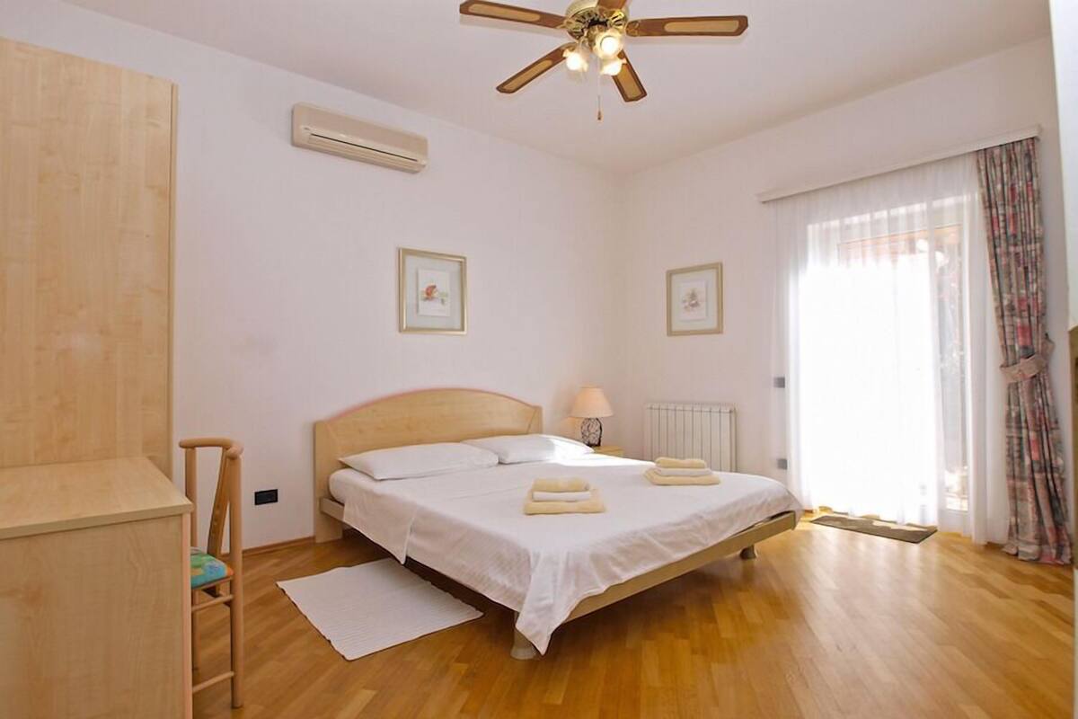 A bedroom with a wooden bed, a ceiling fan, a radiator, and a window with curtains.