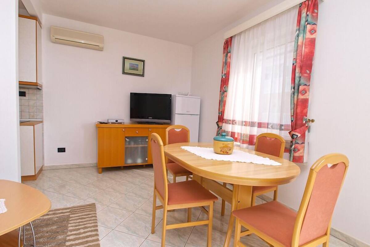 A compact living space with a dining area, a kitchenette, a television, and a window with curtains.
