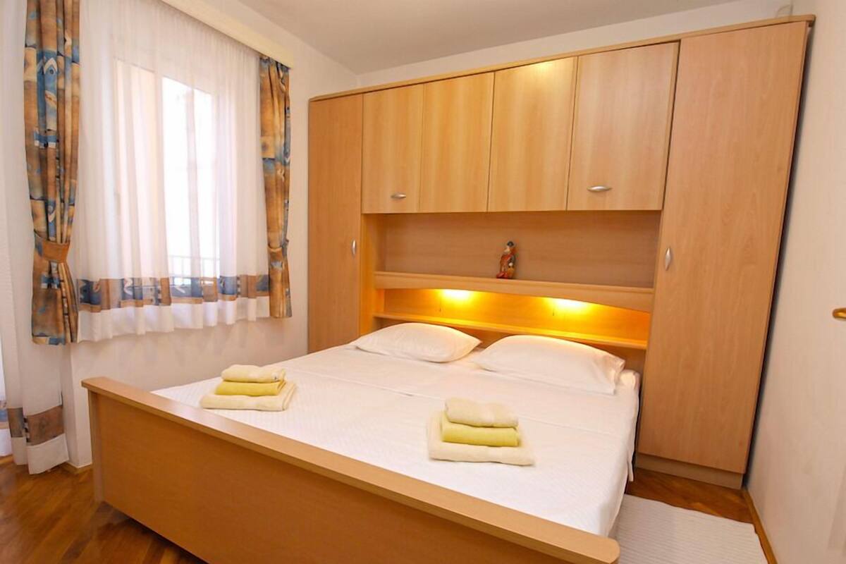 A bedroom with a wooden bed, two pillows, a nightstand, and a wardrobe.