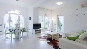 A modern living room with a white sofa, a dining table with chairs, a TV, and a cowhide rug. - Villa Vizula (Medulin)
