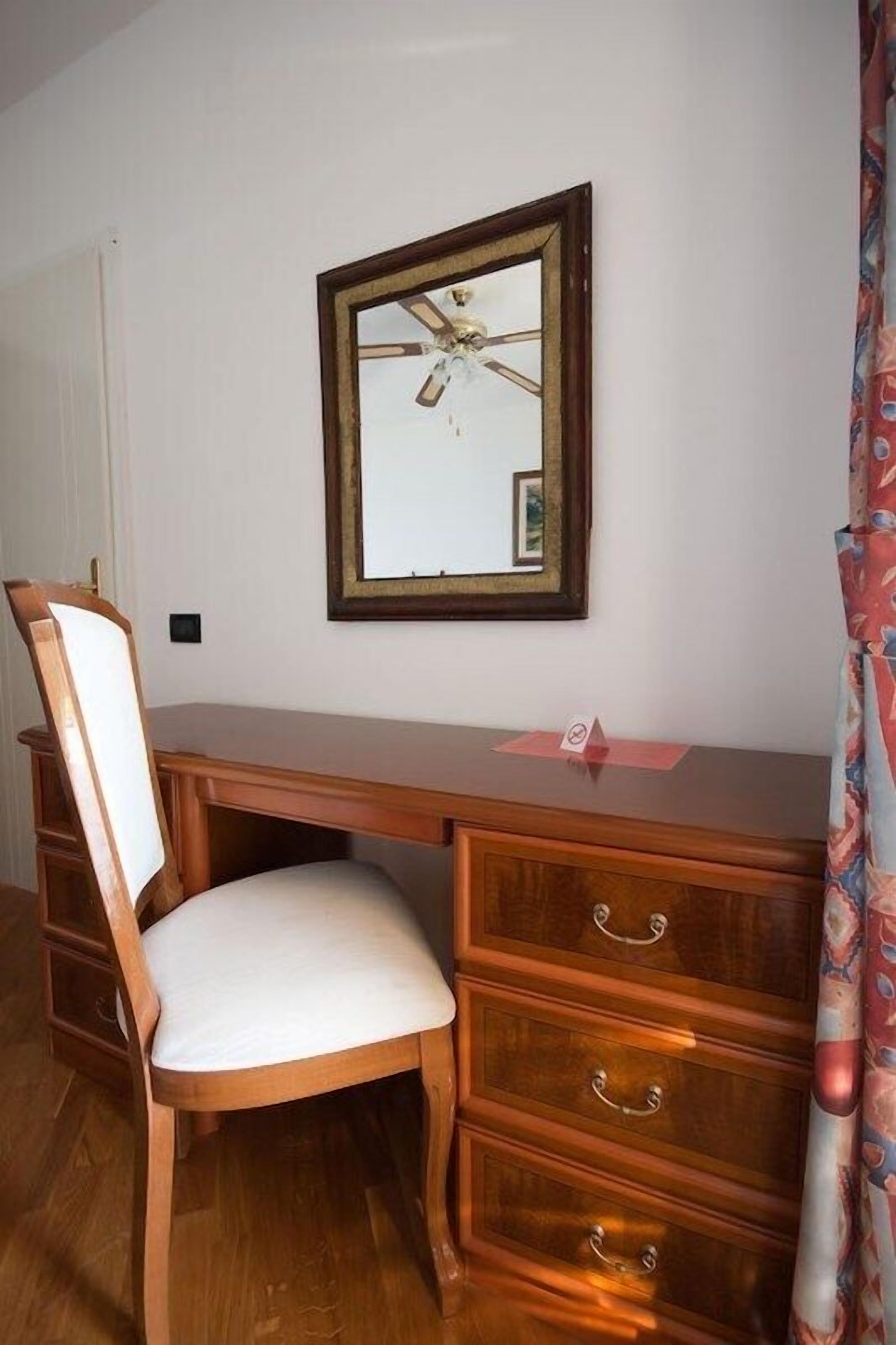 A wooden desk with a chair, a mirror, and a ceiling fan.