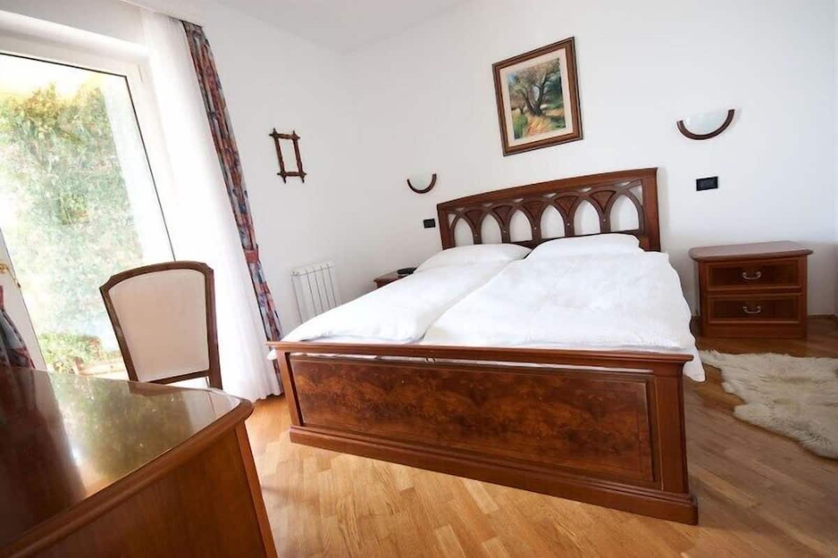 A bedroom with a wooden bed, a desk, a chair, a radiator, a nightstand, and a painting on the wall.