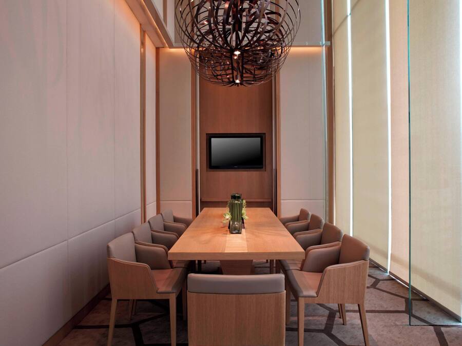Une salle de conférence équipée d’une table en bois, de huit chaises, d’un téléviseur à écran plat et d’un lustre moderne.