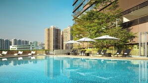 A swimming pool with lounge chairs and umbrellas, surrounded by high-rise buildings.