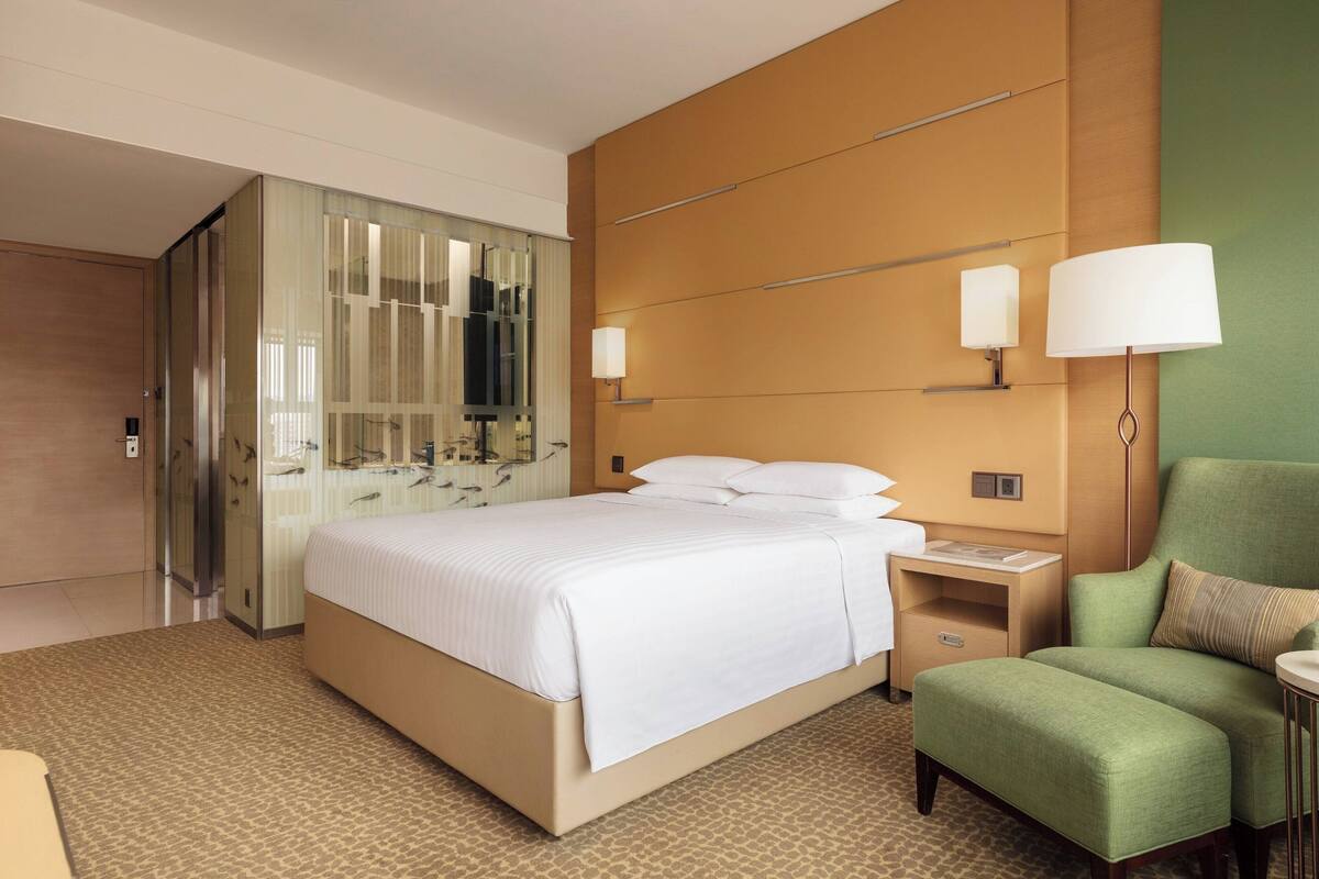 A hotel room with a large bed, a green armchair, a nightstand, and a mirror.