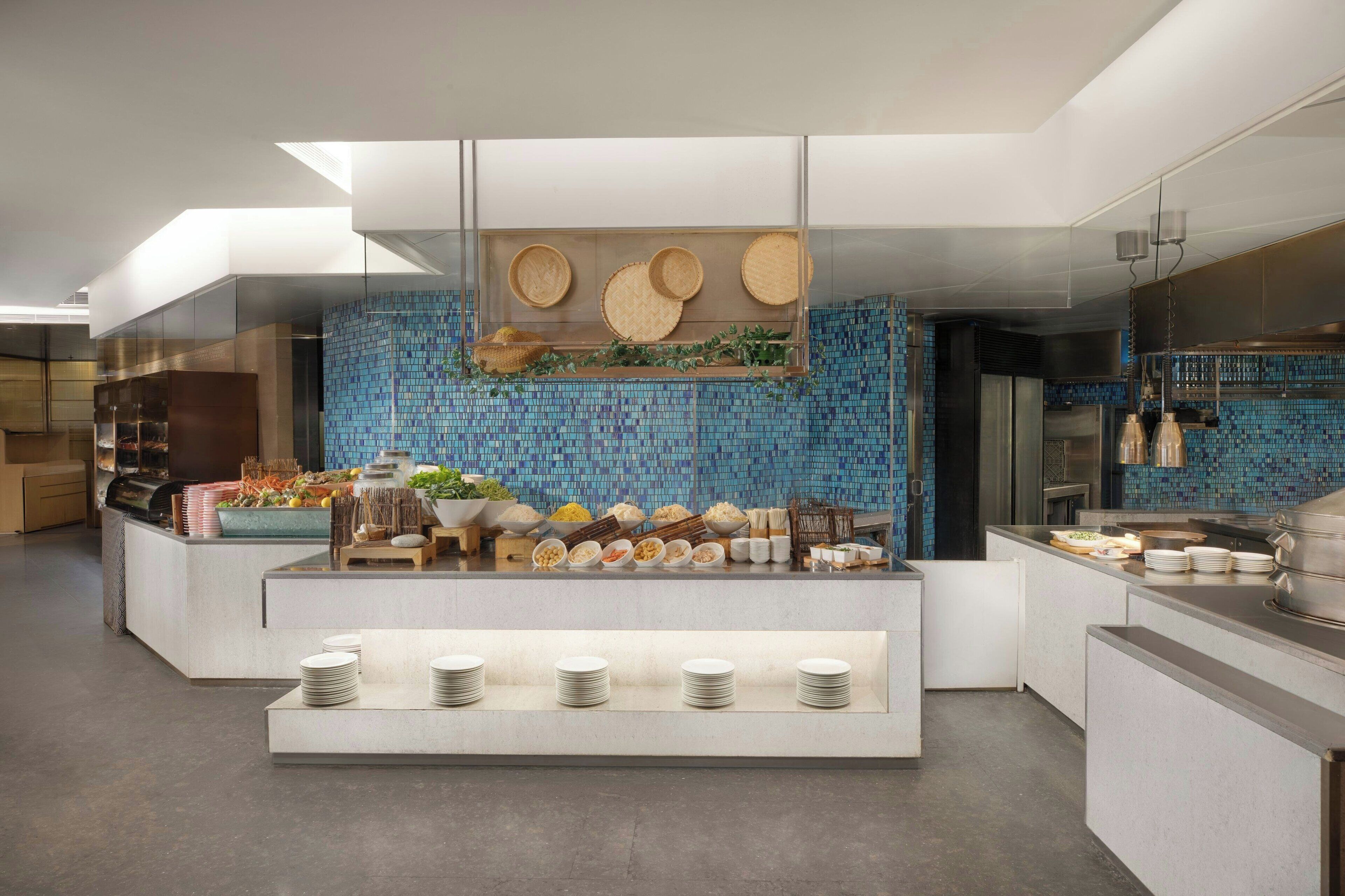 A modern buffet setup with a variety of food items and dishes displayed on a central island, surrounded by neatly arranged plates and bowls.