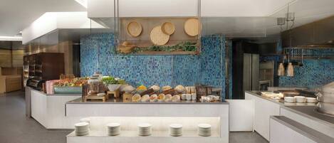 A modern buffet setup with a variety of food items and dishes displayed on a central island, surrounded by neatly arranged plates and bowls.