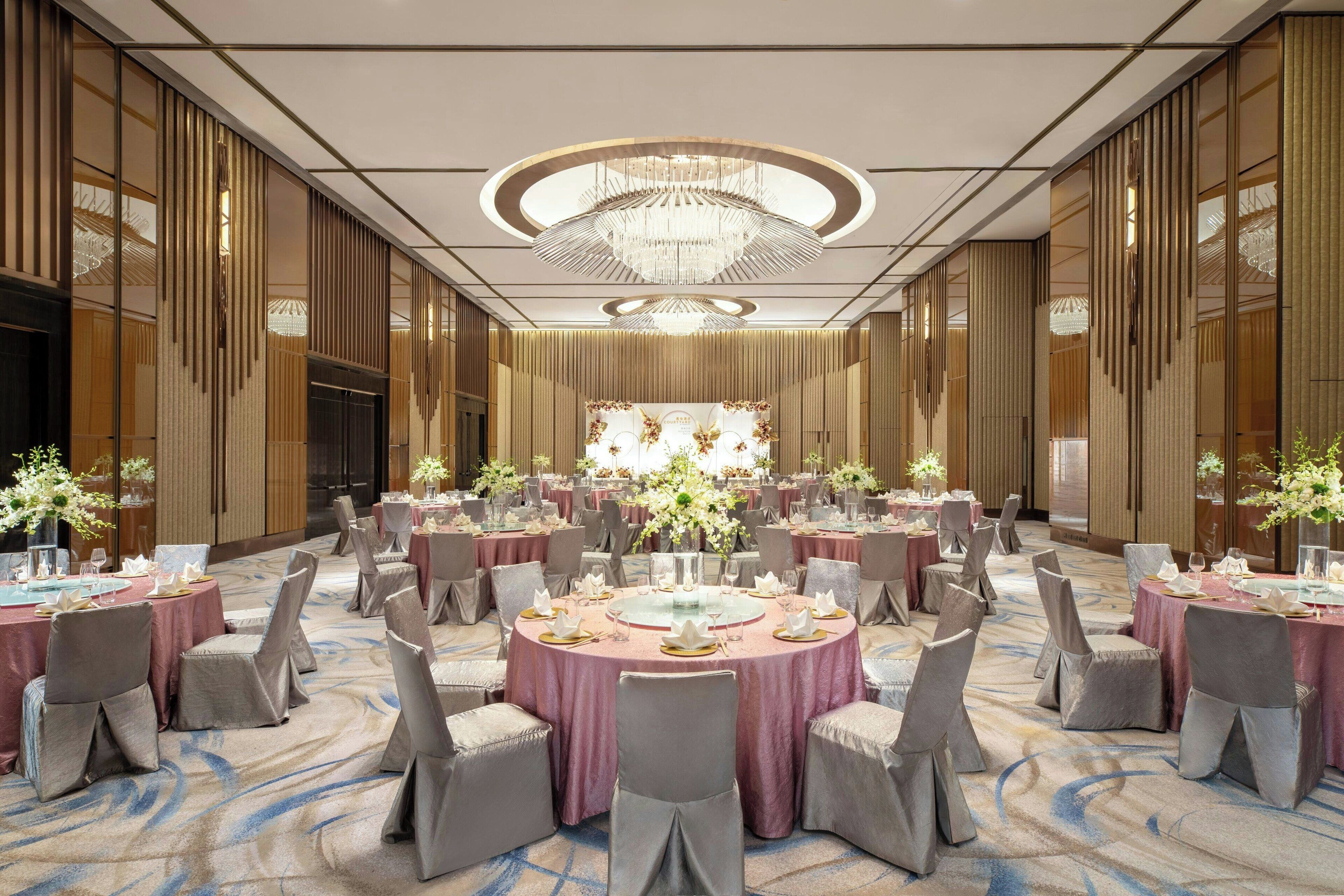 Une salle de banquet avec des tables rondes, des chaises grises et une composition florale au centre.