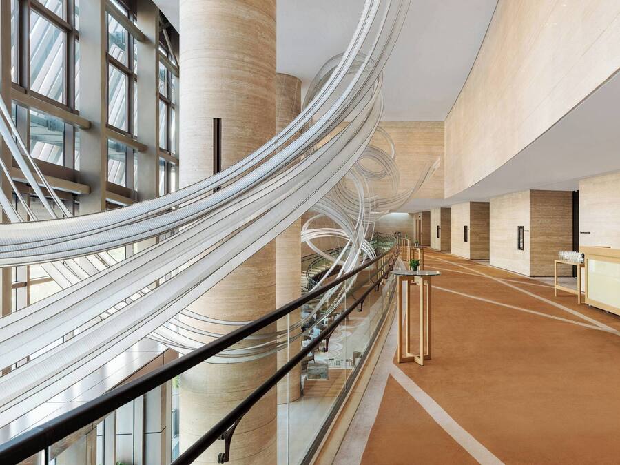Et moderne interiør med en central spiralformet trappe, glasgelændere og et receptionsområde med disk og siddepladser.