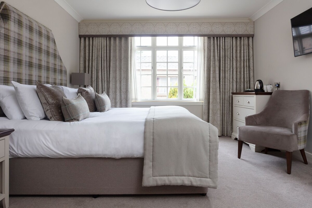 A bedroom with a bed, a chair, a dresser, and a window with curtains.
