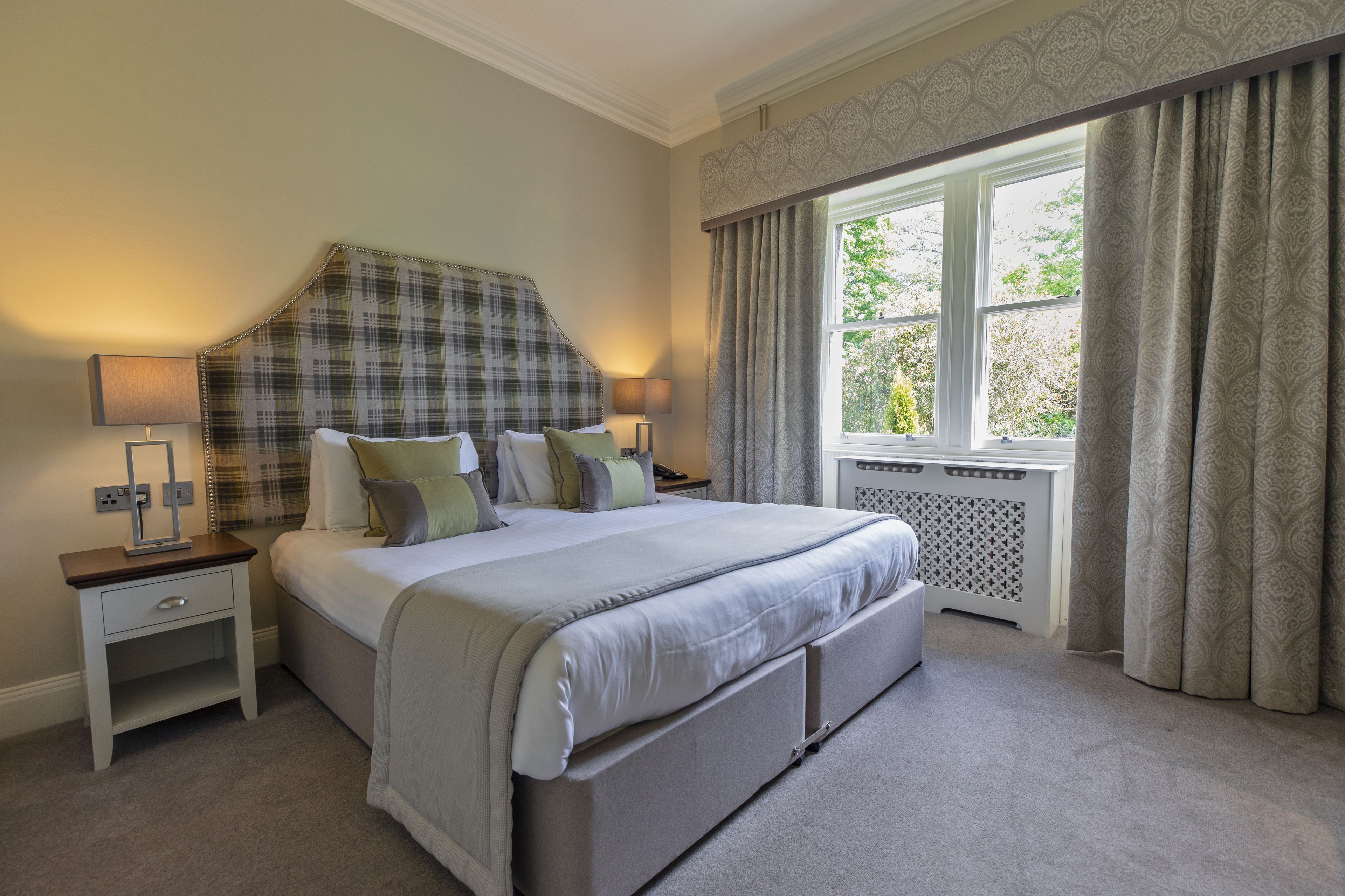 A bedroom with a large bed, two bedside tables, a window with curtains, and a radiator.