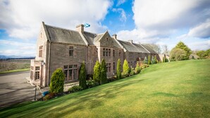 A large stone building with a flag, a well-maintained lawn, and a clear sky. - Murrayshall Country Estate (Perth)