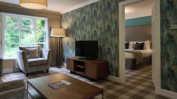 Une chambre d’hôtel avec une grande fenêtre, un téléviseur posé sur un meuble en bois, une moquette à carreaux et un lit recouvert d’une courtepointe à carreaux.