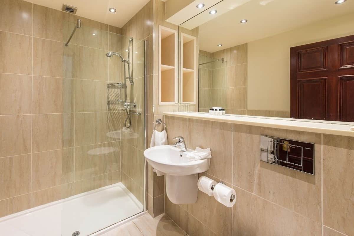 Un baño moderno con ducha de vidrio, lavamanos blanco y un espejo grande.