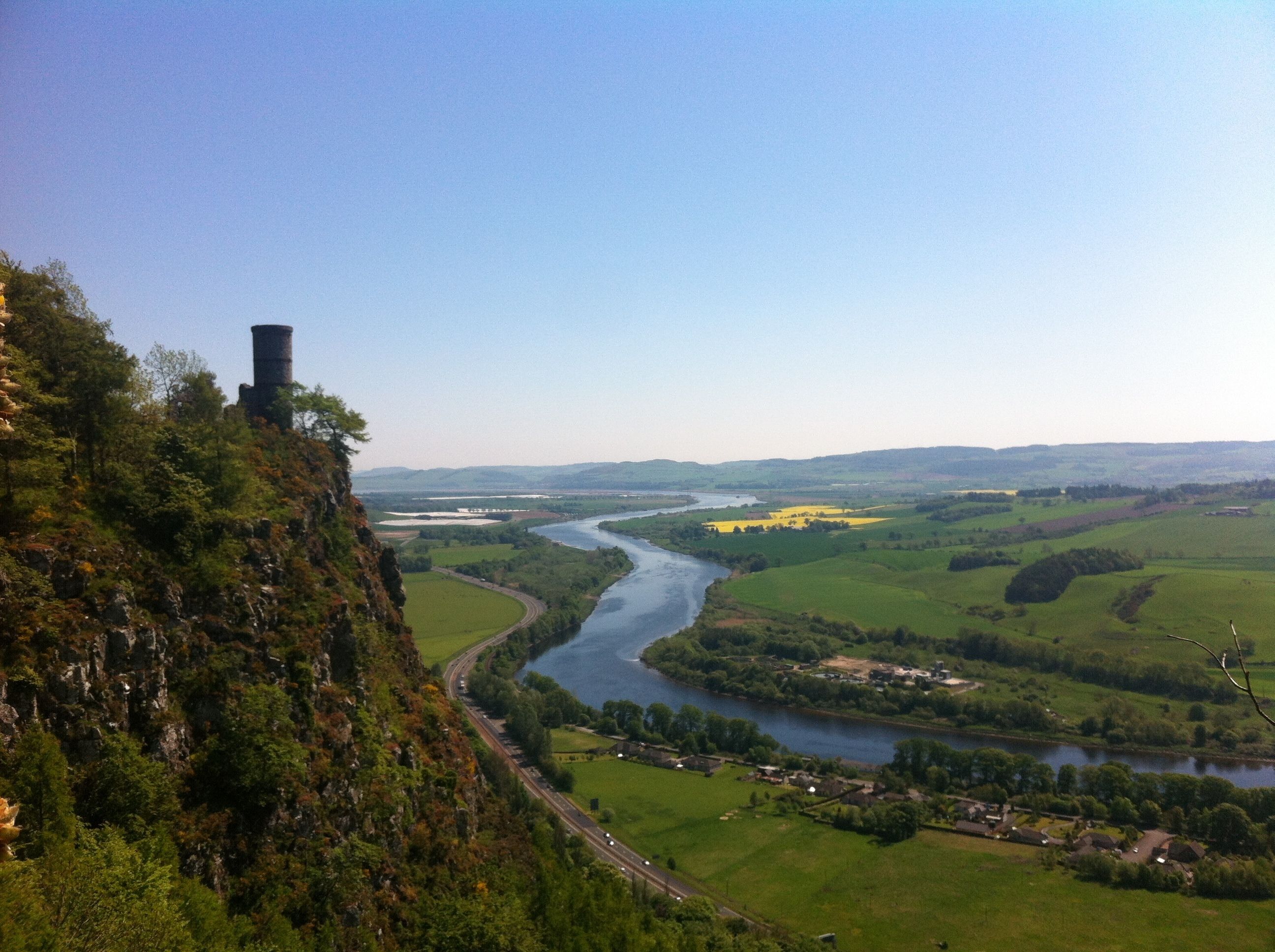 A river winding through a valley with a bridge and a tower on a hill.