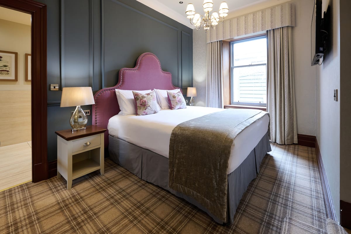 Habitación de hotel con una cama grande, una mesita de noche, una lámpara y una ventana con cortinas.