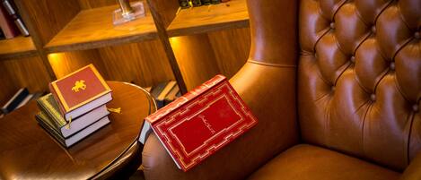 A leather armchair with a book on its armrest and a stack of books on a wooden table.
