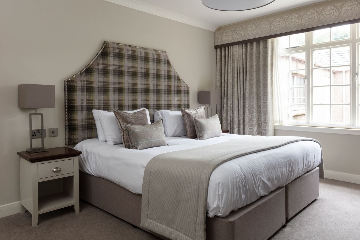 A neatly arranged bedroom with a bed, nightstands, and a window with curtains.