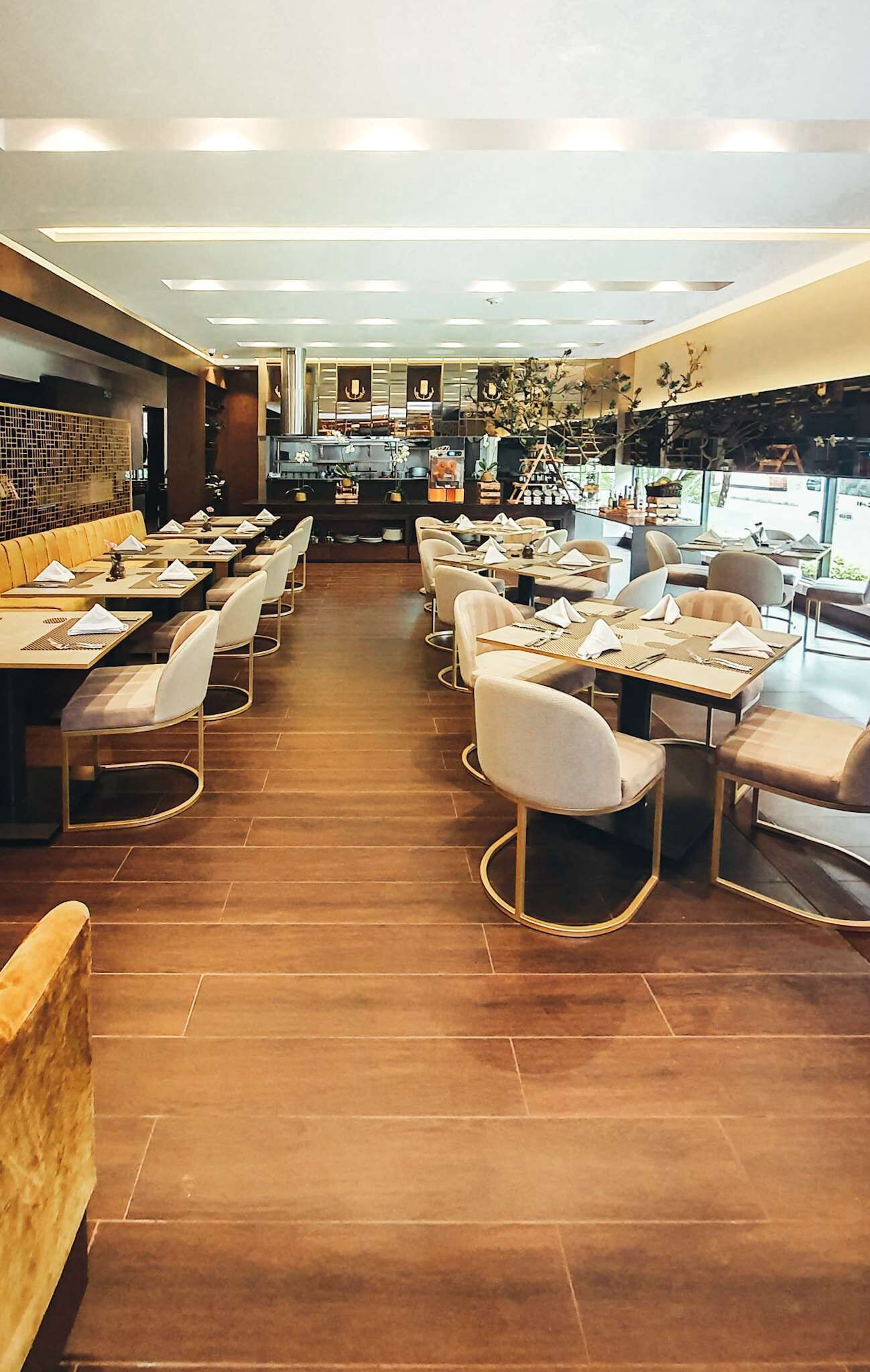 A restaurant with wooden flooring, multiple dining tables and chairs, and a kitchen area in the background.